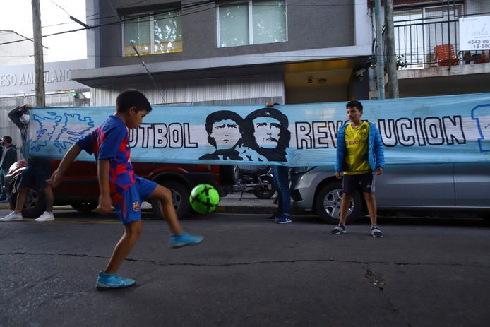 Bij de kliniek waar Maradona wordt geopereerd voetballen jongens bij zijn beeltenis.