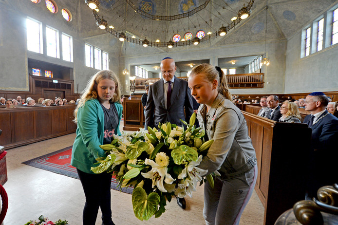Minister Ferdinand Grapperhaus legt samen met leerlingen van de Prinseschool bloemen tijdens de herdenking van de Twentse razzia.